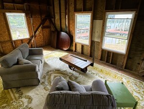 Ein rustikales Holzhäuschen im Inneren mit einer Couch, einem kleinen Tisch und Blick auf einen Steg durch große Fenster.