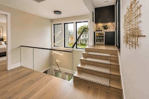 Eine moderne Treppe mit Glastrennwand, Holzboden und einer Küche mit dunklen Schränken und einem Wanddekor.