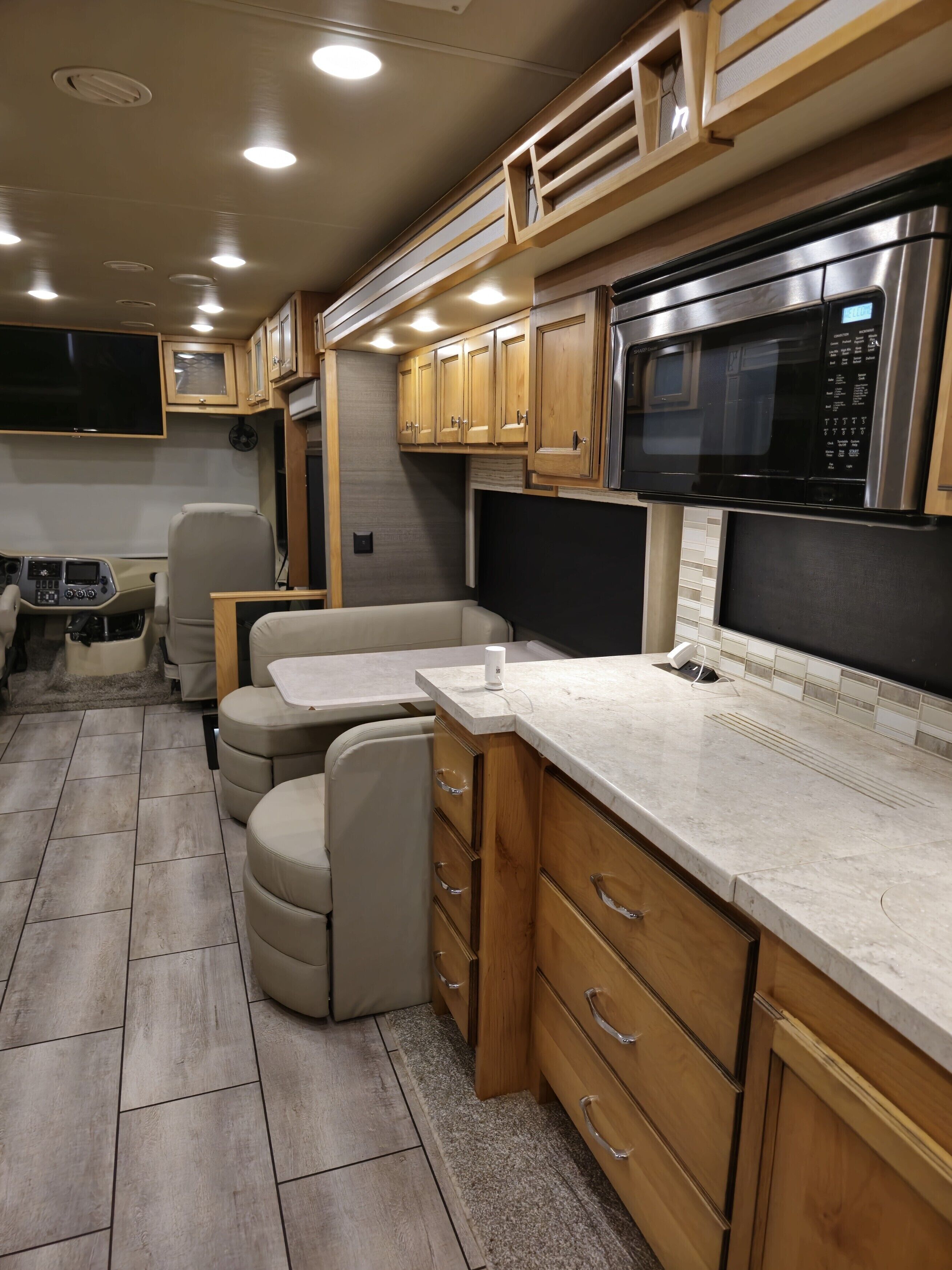 A compact RV kitchen with wooden cabinets, a microwave, a sink, and a seating area.