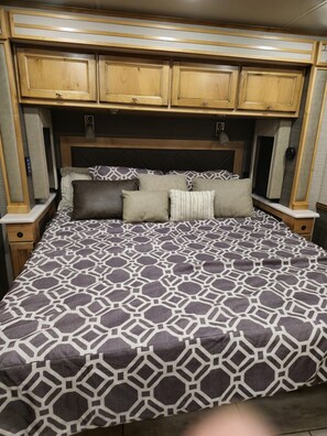 A bedroom with a patterned bedspread, a headboard with built-in cabinets, and a bedside table with a lamp.