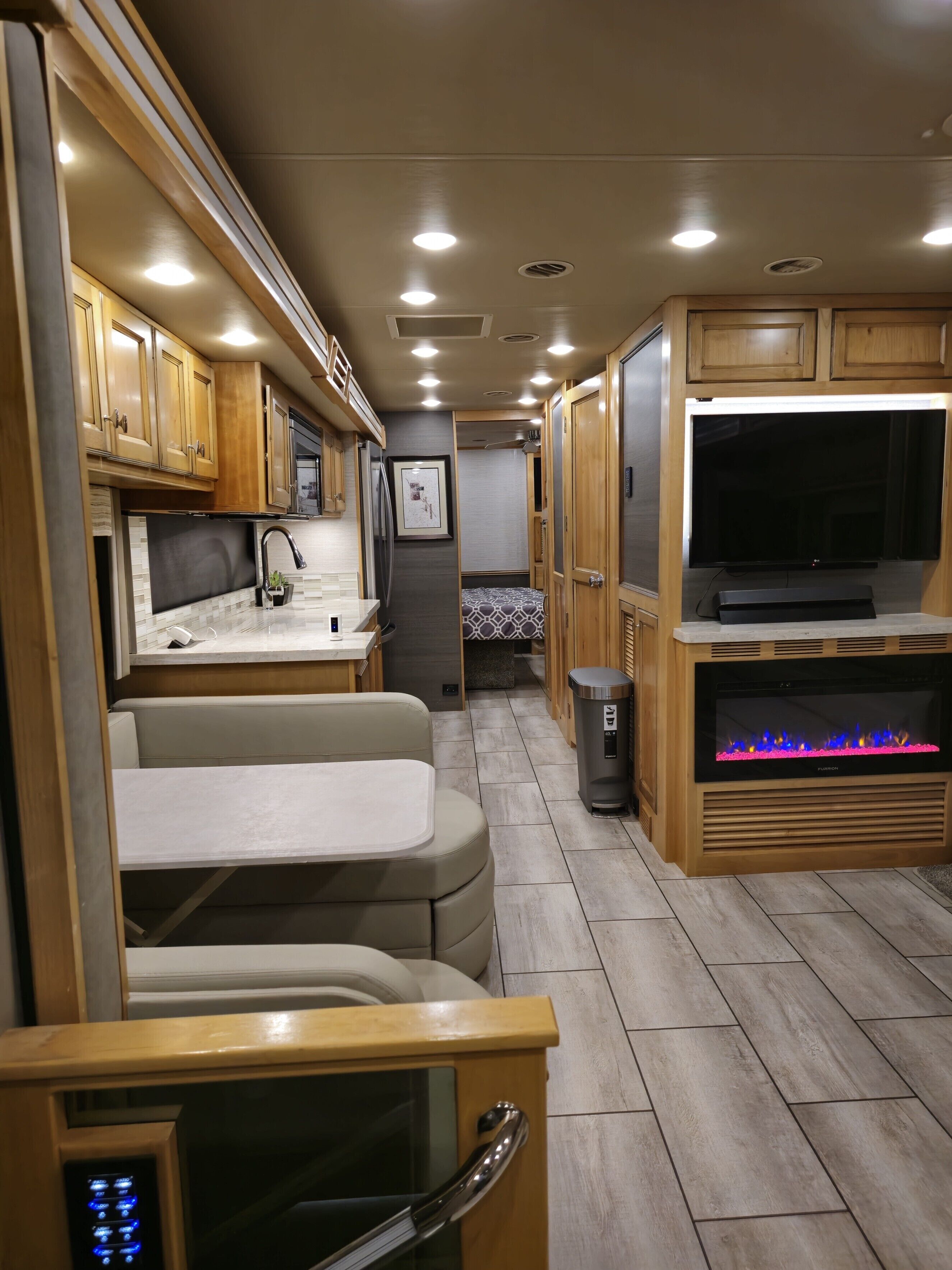 A compact RV interior with a kitchenette, seating area, and a TV.