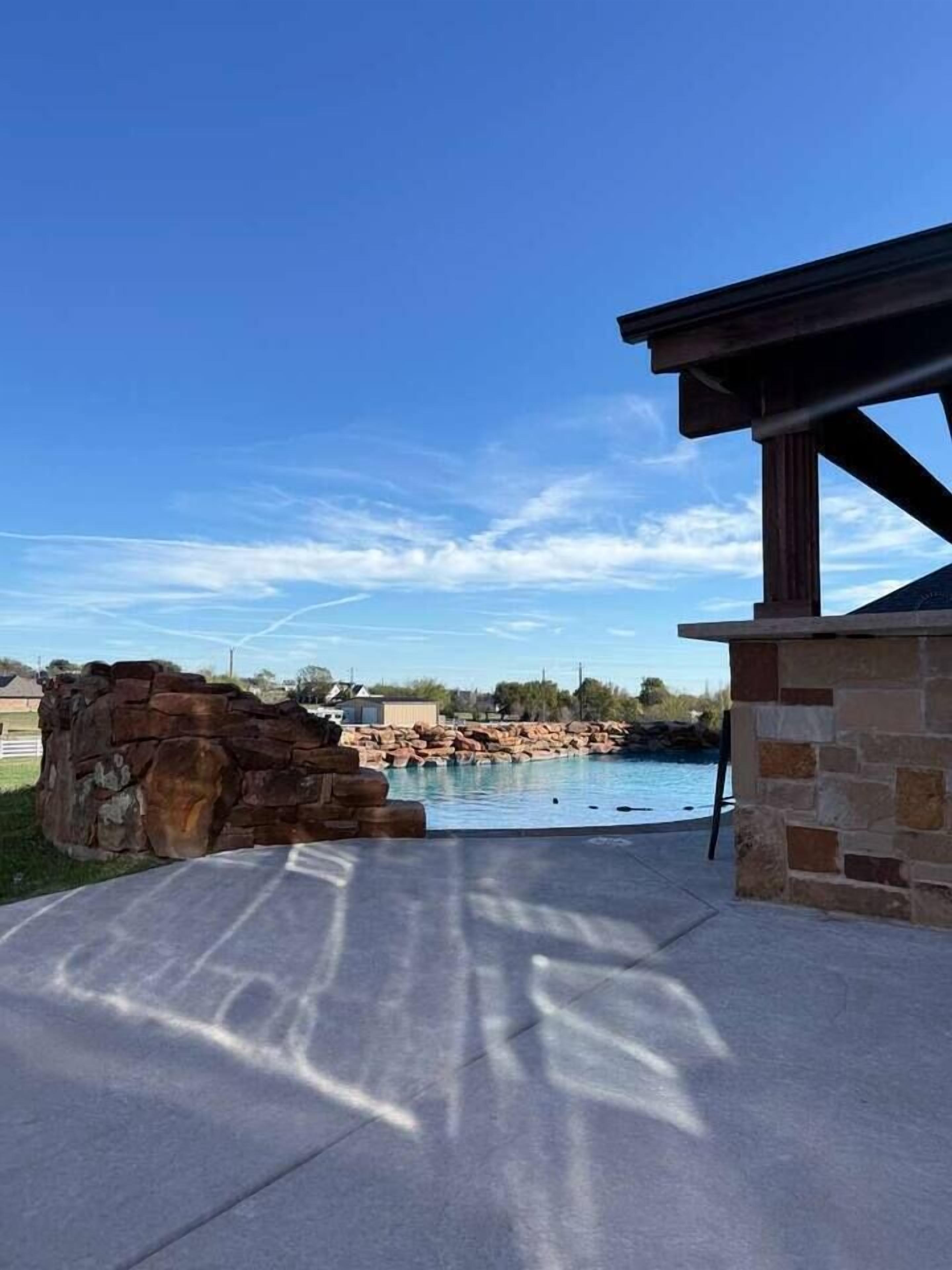 A pool area with a stone structure, a clear sky, and a building with a roof.