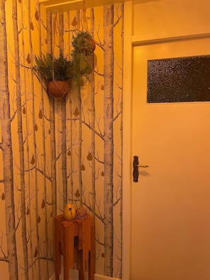 Eine Tür mit einer strukturierten Wand mit Baummuster, einer hängenden Pflanze und einem kleinen Holztisch mit einem gelben Gegenstand.