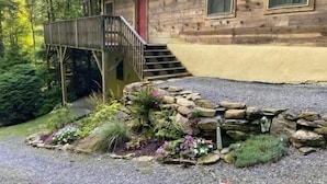 Uma cabana de madeira com porta vermelha, um deck de madeira e uma parede de pedra.