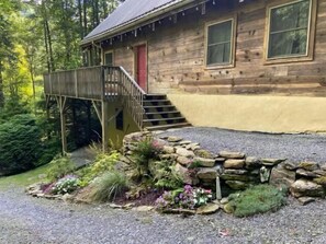 Une cabane en bois avec une porte rouge, une terrasse en bois et un mur en pierre.