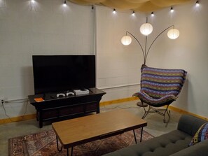 A living room with a TV, gaming console, and a chair.