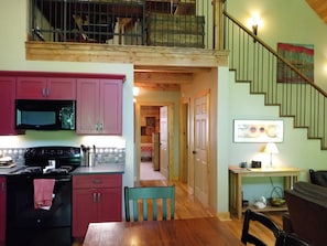 A kitchen with a microwave, stove, and red cabinets. There is a dining table with chairs and a staircase leading to a loft area.