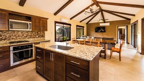 A spacious kitchen with granite countertops, dark wooden cabinets, and a large island. - Casa Quetzal, a charming tropical retreat in Hacienda Pinilla Beach Resort (Santa Cruz)