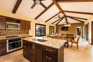 A spacious kitchen with granite countertops, dark wooden cabinets, and a large island. - Casa Quetzal, a charming tropical retreat in Hacienda Pinilla Beach Resort (Santa Cruz)