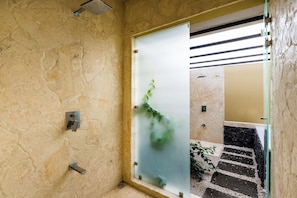 A bathroom with a stone wall, a frosted glass door, a showerhead, and a tiled floor. - Casa Quetzal, a charming tropical retreat in Hacienda Pinilla Beach Resort (Santa Cruz)