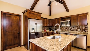 A modern kitchen with dark wood cabinets, stainless steel appliances, a granite countertop, and a ceiling fan. - Casa Quetzal, a charming tropical retreat in Hacienda Pinilla Beach Resort (Santa Cruz)