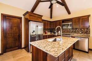 A modern kitchen with dark wood cabinets, stainless steel appliances, a granite countertop, and a ceiling fan. - Casa Quetzal, a charming tropical retreat in Hacienda Pinilla Beach Resort (Santa Cruz)