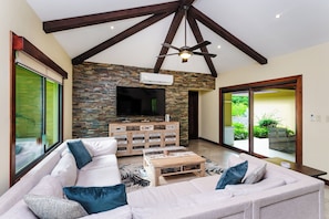 A living room with a large sofa, a coffee table, a flat-screen TV, and a stone wall. - Casa Quetzal, a charming tropical retreat in Hacienda Pinilla Beach Resort (Santa Cruz)