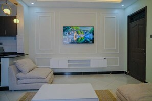 Een woonkamer met een aan de muur bevestigde televisie, een bank, een salontafel en een deur.