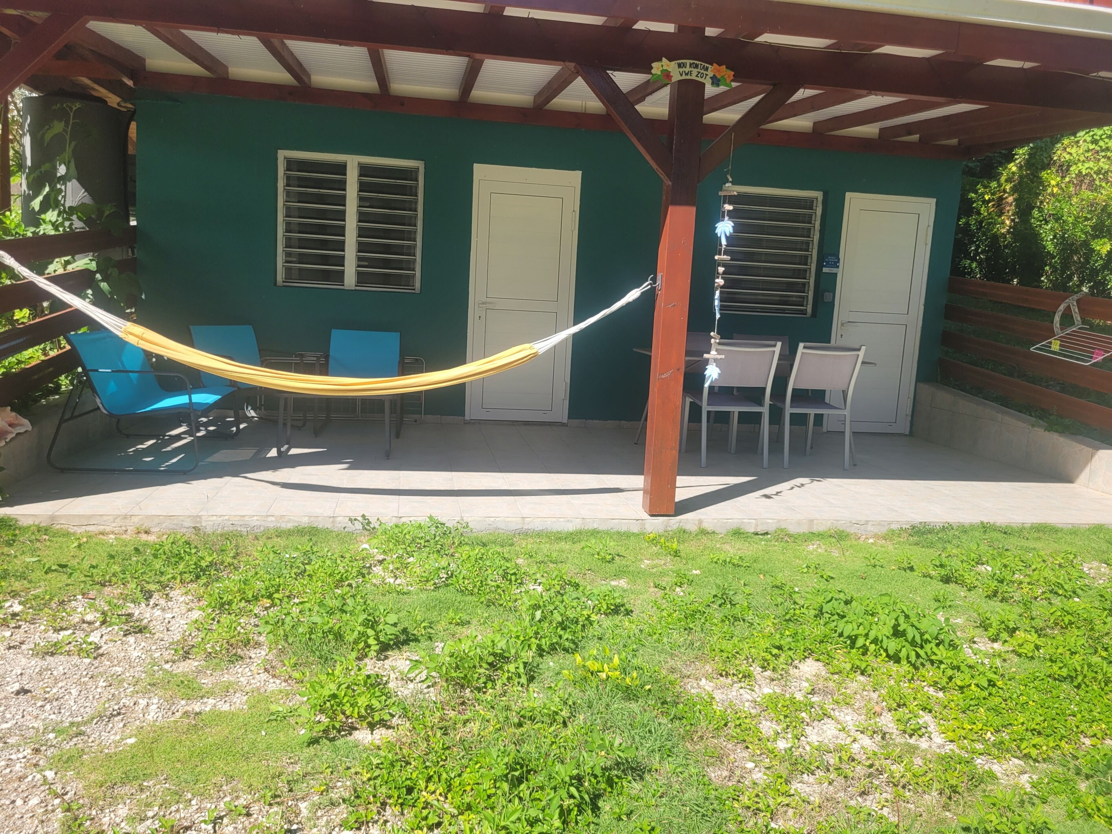 Ein überdachter Patio-Bereich mit einer Hängematte, Sitzgelegenheiten im Freien und einer begrünten Wand mit Fenstern.