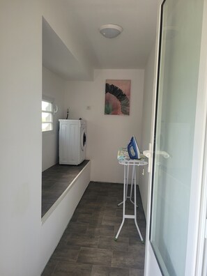Ein Waschbereich mit Waschmaschine, Bügelecke und einem Bild an der Wand.