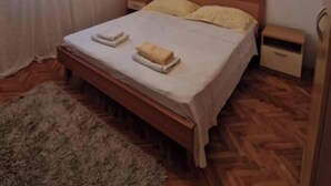 A standard hotel room with a wooden bed, two bedside tables, a small bedside drawer, and a wooden floor. - Two bedroom apartment (Rogoznica)