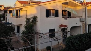 A residential building with multiple balconies, a red-tiled roof, and a garden area with potted plants. - Two bedroom apartment (Rogoznica)
