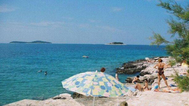 Ein Strand mit Menschen, einer felsigen Küstenlinie und freiem Blick auf das Meer.
