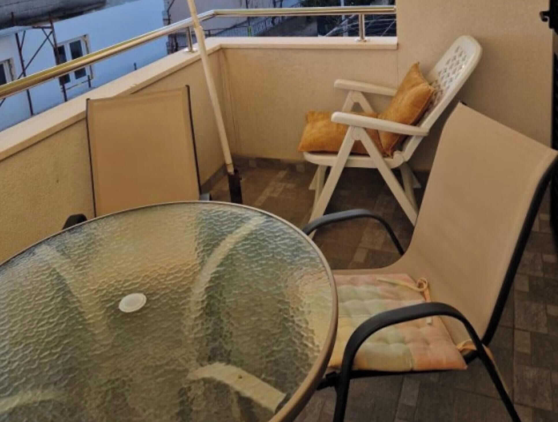 A balcony with a glass table and two chairs, one with a cushion.