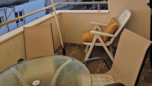 Ein Balkon mit einem Glastisch und zwei Stühlen, einer davon mit Kissen.