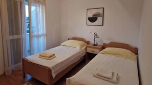 Ein Zimmer mit zwei Einzelbetten, einem Nachttisch mit Lampe, einem gerahmten Bild an der Wand und einem Fenster mit Vorhängen.