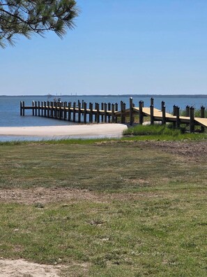 A wooden pier extending into a body of water, surrounded by grassy areas and a clear sky.