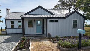 Une maison de plain-pied avec une porte bleue, une boîte aux lettres et des jardinières surélevées.