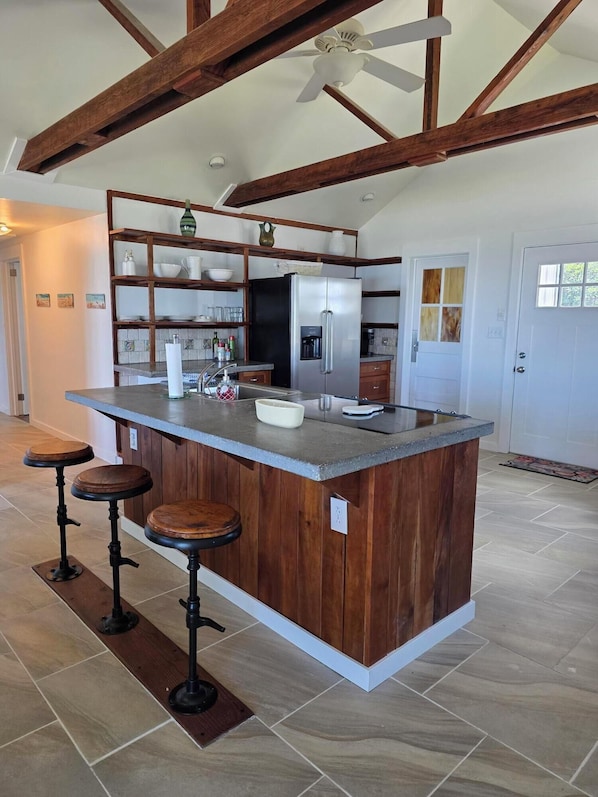 A kitchen with a central island, wooden beams, a ceiling fan, and a refrigerator.