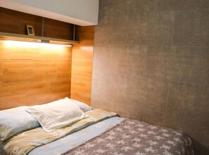 Ein Schlafzimmer mit einem Holz-Kopfteil, einem Bett mit gemusterten Betttextilien und einer Wandleuchte.
