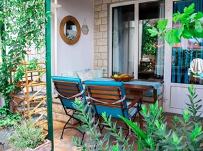 Eine Terrasse mit zwei Holzstühlen, einem Tisch mit Obstkorb und einem Korbstuhl.