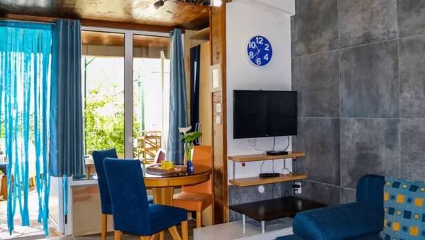 Un soggiorno con televisione, orologio, zona pranzo con sedie e divano.