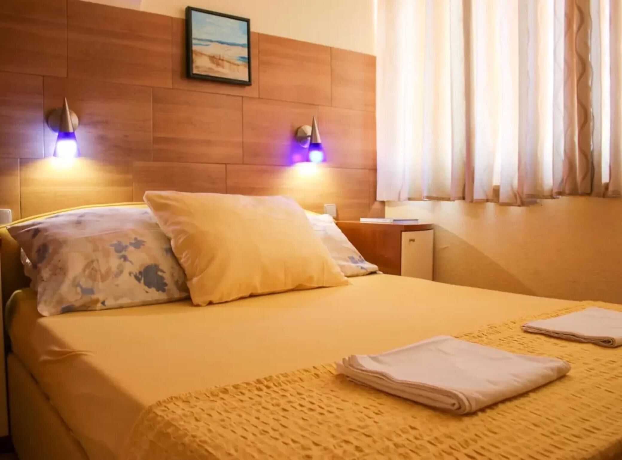 Une chambre d’hôtel avec un lit, des oreillers, une table de chevet, une lampe et une fenêtre avec des rideaux.