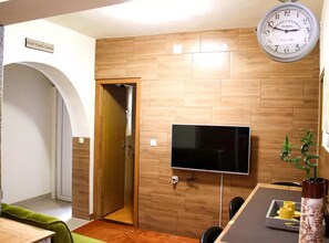 A modern room with a wooden wall, a flat-screen TV, a clock, and a door leading to another room. - two bedroom apartment Paula (Zadar)