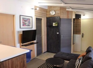 Ein modernes Wohnzimmer mit Flachbildfernseher, einer Couch, einem Couchtisch und einer Tür mit vertikaler Holzpaneelausstattung.