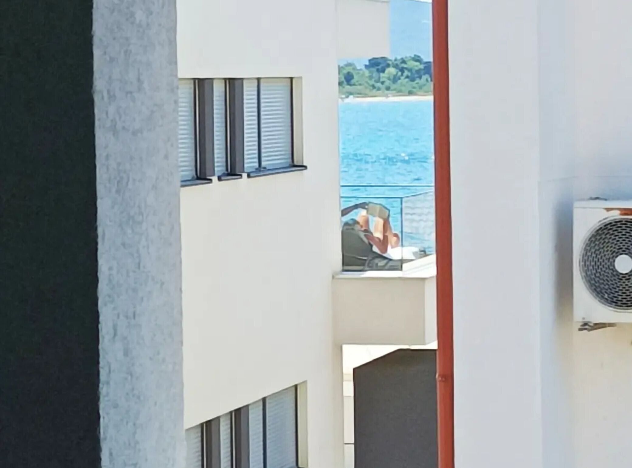 A balcony with a view of the sea and a person reading.