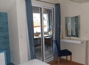 Ein Schlafzimmer mit Schiebeglastür, Schreibtisch, Stuhl, Spiegel und einem weißen Nachttisch.