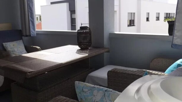 A balcony with wicker furniture, a hanging lantern, and a view of modern buildings. - two bedroom apartment Ljiljana (Zadar)