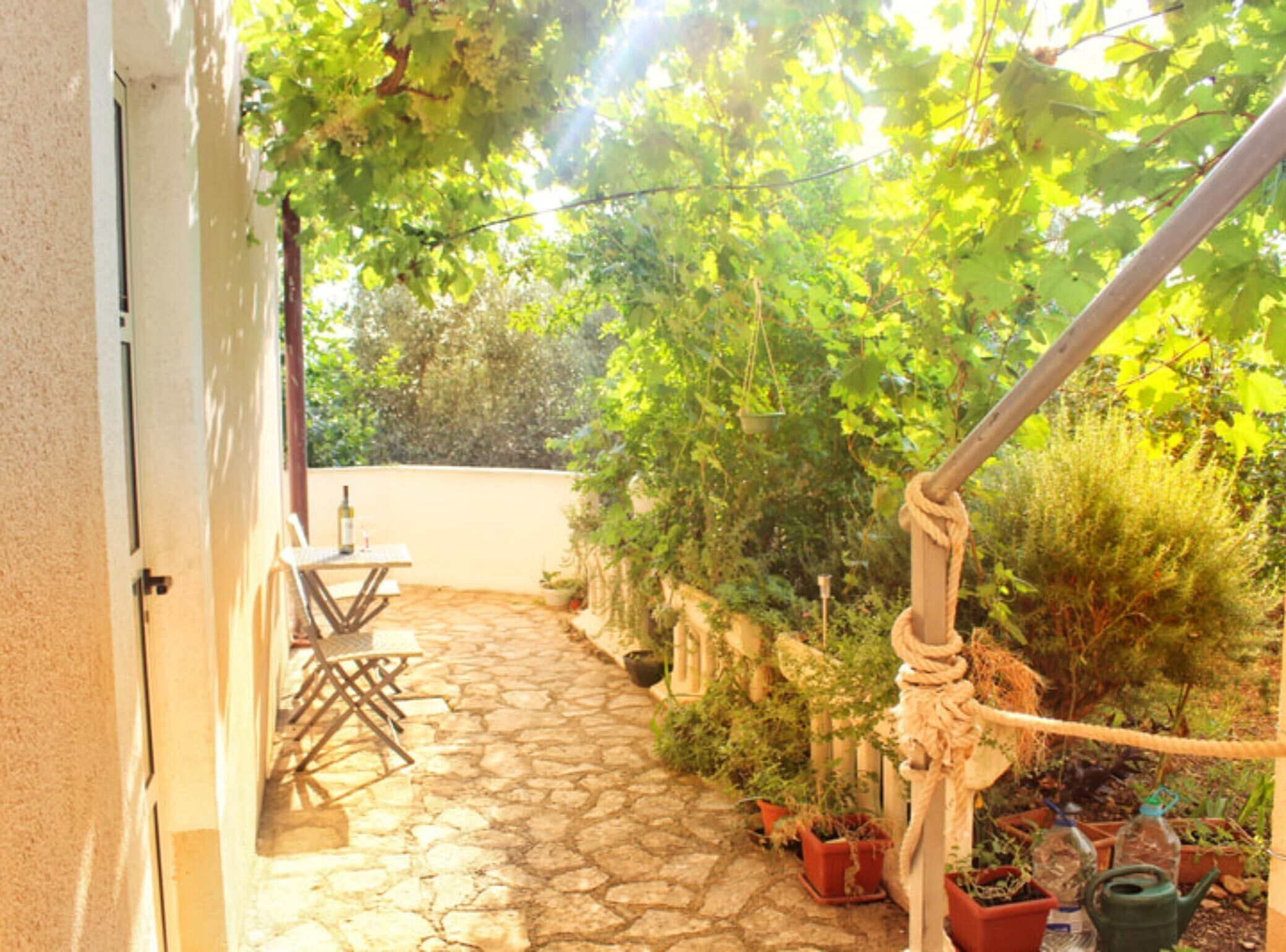A stone-paved patio with a table and chairs, surrounded by potted plants and a rope barrier.