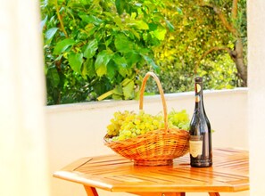 A wicker basket with grapes and a bottle of wine on a wooden table. - one bedroom apartment Olea (Podgora)