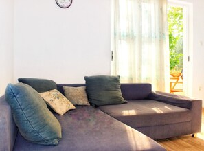 Ein Wohnzimmer mit einer Couch, Kissen, einer Uhr und Blick durch ein Fenster.