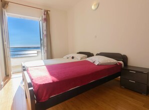 Ein Schlafzimmer mit Bett, Nachttisch, einem Fenster mit Vorhängen und Blick aufs Meer.