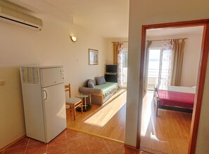Ein kleines Zimmer mit Kühlschrank, Esstisch, Sofa, Bett und Fernseher.