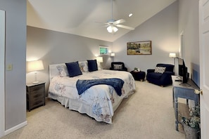 A bedroom with a bed, nightstands, a desk, a chair, a ceiling fan, and a painting on the wall.