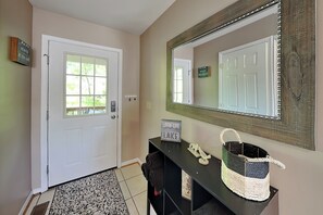 A hallway with a white door, a large mirror, a black console table with a woven basket, and a sign that reads 'LOVIN' LIFE.'