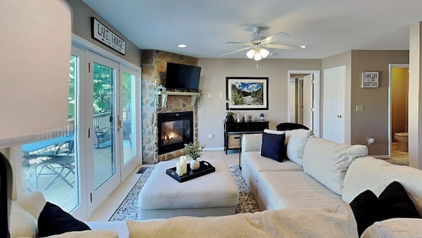 A living room with a fireplace, a ceiling fan, and a sliding glass door leading to an outdoor area. - The Fairway Retreat (Oakland)