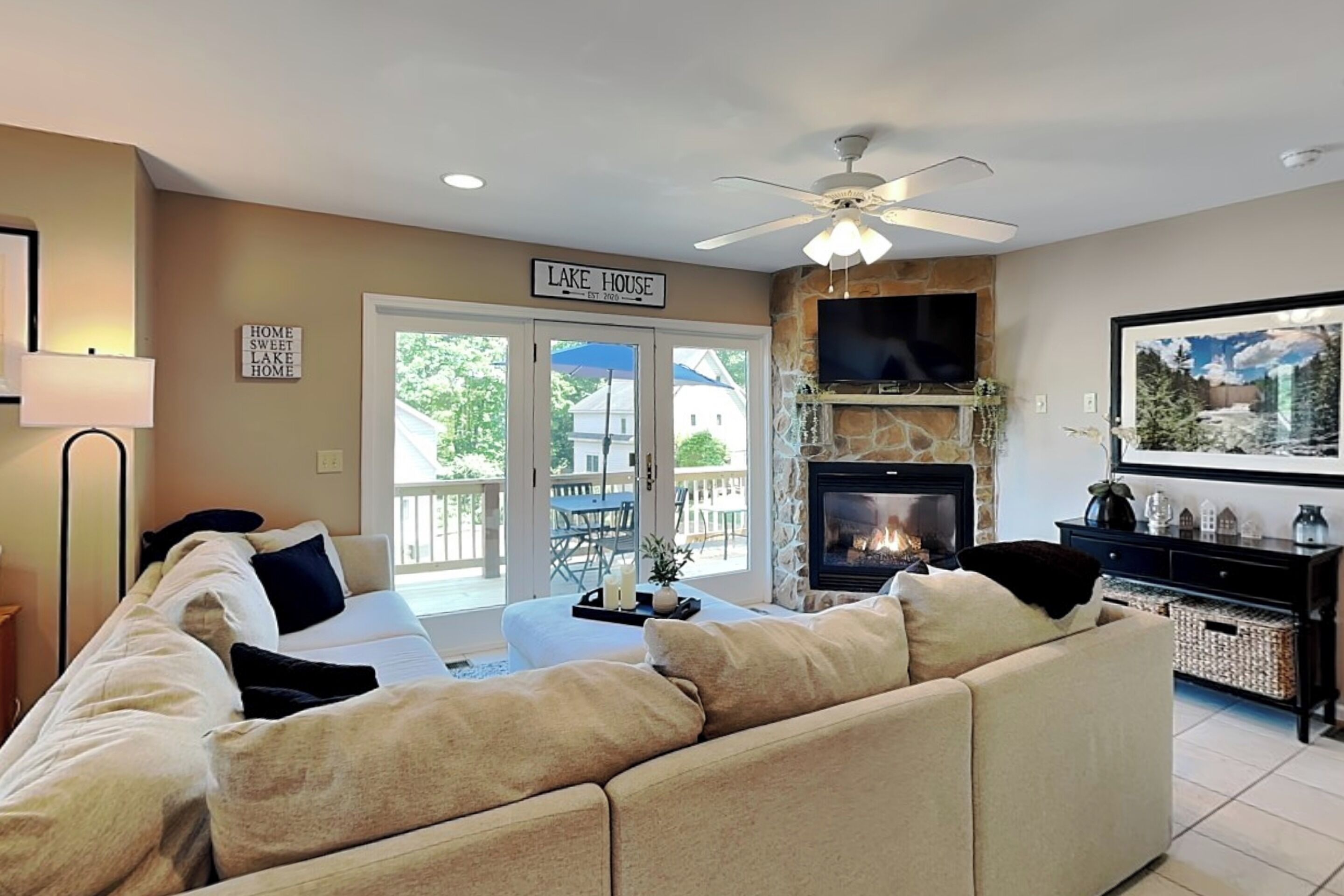 A living room with a beige sofa, a fireplace, a television, and a ceiling fan.
