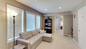 A living room with a sectional sofa, a bookshelf, and a lamp. - The Fairway Retreat (Oakland)
