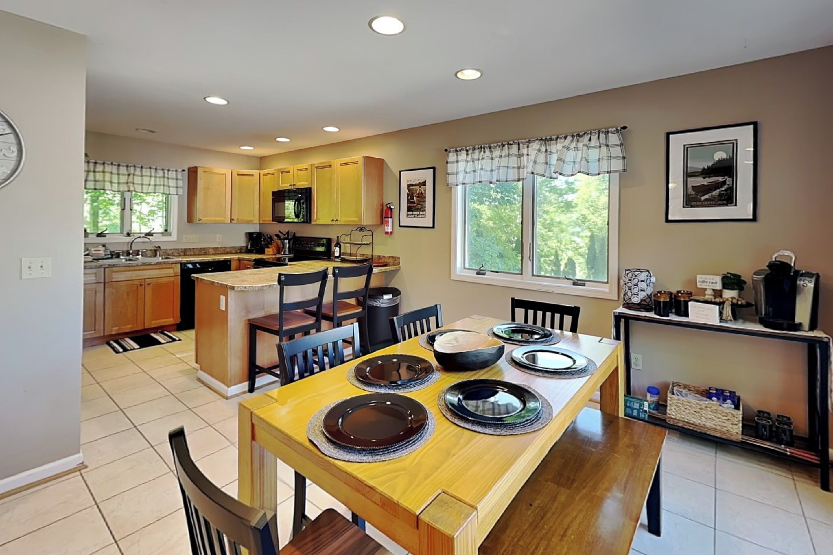A kitchen with wooden cabinets, a dining table set with plates, and a window with a view of trees.