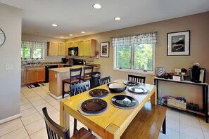 Una cocina con armarios de madera, una mesa de comedor dispuesta con platos, y un ventanal con vistas a árboles.